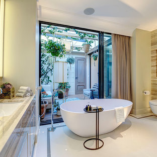Inspiration for a medium sized contemporary ensuite bathroom in London with beaded cabinets, beige cabinets, a freestanding bath, a walk-in shower, a wall mounted toilet, brown tiles, marble tiles, beige walls, porcelain flooring, an integrated sink, marble worktops, beige floors and a hinged door.