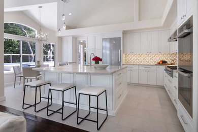 Example of a large transitional l-shaped porcelain tile, gray floor and vaulted ceiling open concept kitchen design in San Francisco with an undermount sink, recessed-panel cabinets, white cabinets, quartzite countertops, multicolored backsplash, marble backsplash, stainless steel appliances, an island and white countertops