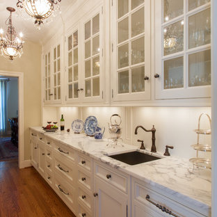 Large traditional kitchen pantry inspiration - Kitchen pantry - large traditional galley medium tone wood floor kitchen pantry idea in St Louis with glass-front cabinets, white cabinets, marble countertops, white backsplash and paneled appliances