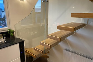 Cette image montre un petit escalier sans contremarche design en U avec des marches en bois et un garde-corps en verre.