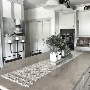 Ispirazione per una grande cucina country con paraspruzzi in travertino, elettrodomestici neri, parquet chiaro, isola, pavimento bianco, top grigio, lavello a doppia vasca, ante bianche, top in cemento e paraspruzzi grigio