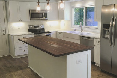 Inspiration for a mid-sized country l-shaped laminate floor and brown floor eat-in kitchen remodel in Minneapolis with a farmhouse sink, shaker cabinets, white cabinets, wood countertops, white backsplash, ceramic backsplash, stainless steel appliances, an island and brown countertops