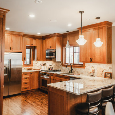 Inspiration for a mid-sized craftsman u-shaped dark wood floor and brown floor eat-in kitchen remodel in Minneapolis with an undermount sink, recessed-panel cabinets, medium tone wood cabinets, granite countertops, beige backsplash, stone tile backsplash, stainless steel appliances, a peninsula and beige countertops