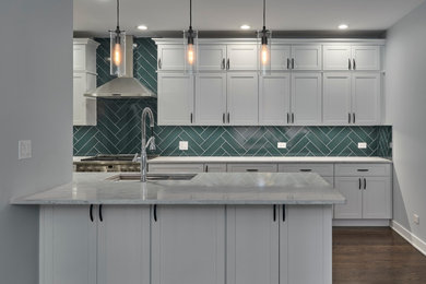 Example of a mid-sized transitional galley open concept kitchen design in Chicago with recessed-panel cabinets, white cabinets, quartzite countertops, green backsplash, stainless steel appliances, a peninsula and white countertops