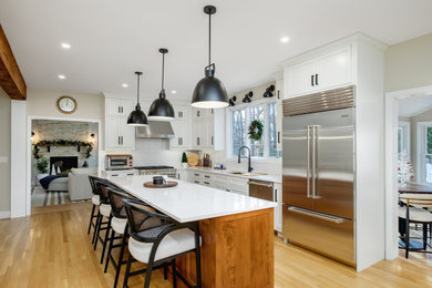 Eat-in kitchen - large transitional u-shaped light wood floor eat-in kitchen idea in Boston with an undermount sink, recessed-panel cabinets, white cabinets, quartz countertops, white backsplash, ceramic backsplash, stainless steel appliances, an island and white countertops