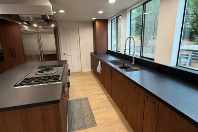 Inspiration for a contemporary beige floor eat-in kitchen remodel with an undermount sink, flat-panel cabinets, brown cabinets, black backsplash, an island and black countertops