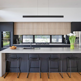 Design ideas for a beach style kitchen in Sunshine Coast with an undermount sink, flat-panel cabinets, black cabinets, window splashback, stainless steel appliances, medium hardwood floors, with island and white benchtop.