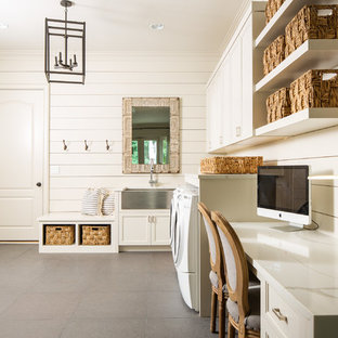 アトランタの中サイズのカントリー風おしゃれな家事室 (エプロンフロントシンク、落し込みパネル扉のキャビネット、白いキャビネット、クオーツストーンカウンター、白い壁、コンクリートの床、左右配置の洗濯機・乾燥機、グレーの床、白いキッチンカウンター) の写真