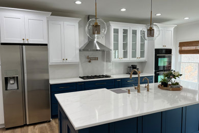 アトランタにある高級な中くらいなトランジショナルスタイルのおしゃれなキッチン (エプロンフロントシンク、シェーカースタイル扉のキャビネット、青いキャビネット、クオーツストーンカウンター、白いキッチンパネル、クオーツストーンのキッチンパネル、シルバーの調理設備、クッションフロア、茶色い床、白いキッチンカウンター) の写真