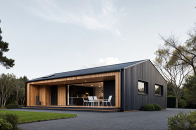 Medium sized and black modern bungalow rear tiny house in London with metal cladding, a pitched roof, a metal roof and a black roof.