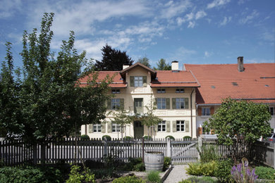 Idée de décoration pour une façade de maison jaune en stuc à un étage avec un toit à deux pans, un toit en tuile et un toit rouge.