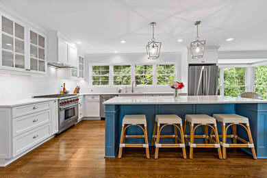 Example of a large country l-shaped medium tone wood floor and brown floor eat-in kitchen design in Dallas with a single-bowl sink, recessed-panel cabinets, white cabinets, quartz countertops, white backsplash, subway tile backsplash, stainless steel appliances, an island and white countertops