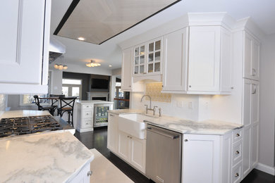 Mid-sized transitional galley dark wood floor and brown floor kitchen photo in St Louis with a farmhouse sink, shaker cabinets, white cabinets, marble countertops, white backsplash, subway tile backsplash, stainless steel appliances, an island and gray countertops