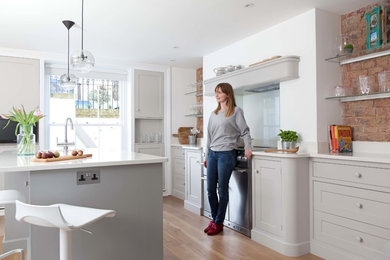 This is an example of a mid-sized contemporary galley eat-in kitchen in London with shaker cabinets, grey cabinets, quartzite benchtops, white splashback, glass sheet splashback, stainless steel appliances, painted wood floors and with island.