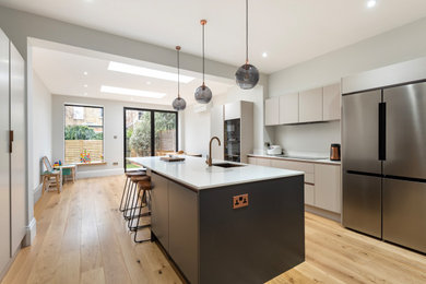 Inspiration for a medium sized contemporary grey and black kitchen/diner in London with a built-in sink, flat-panel cabinets, grey cabinets, quartz worktops, grey splashback, engineered quartz splashback, stainless steel appliances, light hardwood flooring, an island, white worktops, a drop ceiling and feature lighting.