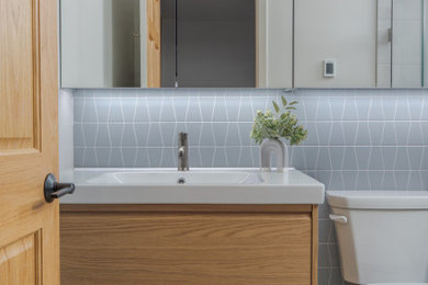 Trendy gray tile and mosaic tile gray floor and single-sink bathroom photo in Minneapolis with flat-panel cabinets, light wood cabinets, a two-piece toilet, an integrated sink, white countertops and a floating vanity