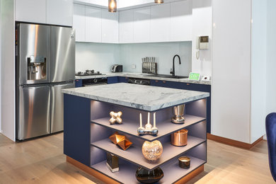 Small contemporary l-shaped kitchen pantry in Melbourne with a drop-in sink, flat-panel cabinets, blue cabinets, quartz benchtops, white splashback, glass sheet splashback, stainless steel appliances, medium hardwood floors, with island, beige floor and white benchtop.