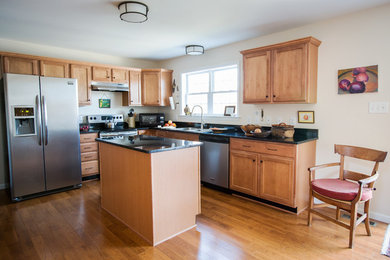 This is an example of a mid-sized eclectic l-shaped eat-in kitchen in New York with a drop-in sink, recessed-panel cabinets, medium wood cabinets, granite benchtops, stainless steel appliances, medium hardwood floors and with island.