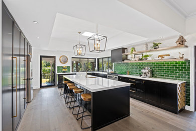 Photo of a large traditional l-shaped kitchen pantry in Gold Coast - Tweed with a farmhouse sink, flat-panel cabinets, black cabinets, quartz benchtops, green splashback, ceramic splashback, stainless steel appliances, medium hardwood floors, with island, brown floor, white benchtop and coffered.