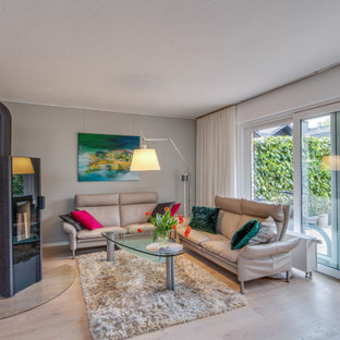 ボンの巨大なモダンスタイルのLDKの画像 (グレーの壁、淡色無垢フローリング、薪ストーブ、石材の暖炉まわり)