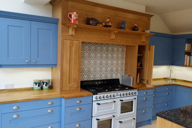 This is an example of a large traditional kitchen in Dorset with a single-bowl sink, blue cabinets, wood benchtops, cement tile splashback, coloured appliances, travertine floors and beige floor.