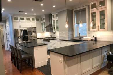 Photo of a large contemporary u-shaped eat-in kitchen in New York with an undermount sink, shaker cabinets, white cabinets, solid surface benchtops, grey splashback, stone tile splashback, stainless steel appliances, dark hardwood floors, with island, brown floor, black benchtop and vaulted.