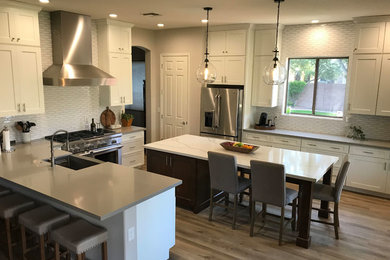 Open concept kitchen - mid-sized modern u-shaped porcelain tile and brown floor open concept kitchen idea in Phoenix with a farmhouse sink, shaker cabinets, white cabinets, quartz countertops, white backsplash, subway tile backsplash, stainless steel appliances, an island and gray countertops