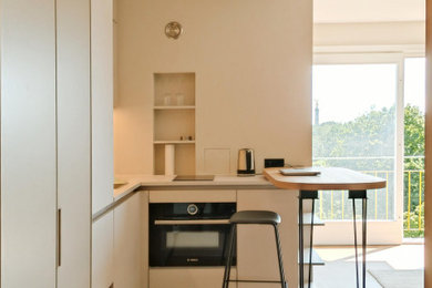 Kleine Mid-Century Küche in L-Form mit Waschbecken, flächenbündigen Schrankfronten, beigen Schränken, Arbeitsplatte aus Holz, Küchenrückwand in Beige, schwarzen Elektrogeräten, Korkboden, braunem Boden, grauer Arbeitsplatte und eingelassener Decke in Berlin