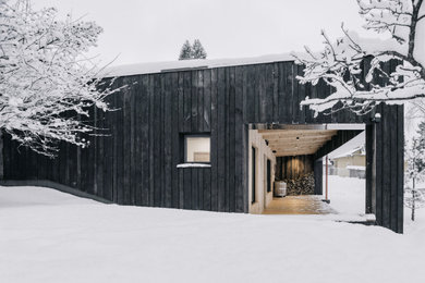 На фото: маленький, одноэтажный, деревянный, черный частный загородный дом в скандинавском стиле с плоской крышей и зеленой крышей для на участке и в саду