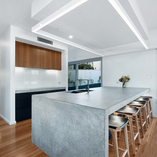 Large modern kitchen pantry photos - Inspiration for a large modern galley medium tone wood floor and brown floor kitchen pantry remodel in Newcastle - Maitland with a drop-in sink, flat-panel cabinets, black cabinets, concrete countertops, white backsplash, glass sheet backsplash, black appliances, an island and gray countertops