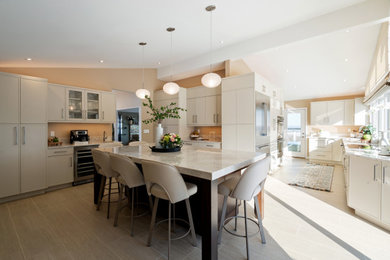 Example of a large trendy porcelain tile and beige floor enclosed kitchen design in Other with an undermount sink, flat-panel cabinets, beige cabinets, quartzite countertops, stainless steel appliances, an island and beige countertops