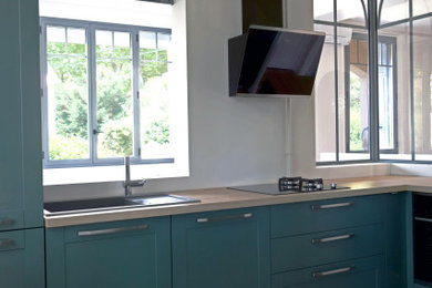 Exemple d'une cuisine tendance en U avec des portes de placards vertess, un plan de travail en bois, un électroménager noir et un sol en terrazzo.