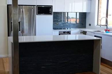 Photo of a mid-sized contemporary l-shaped eat-in kitchen in Perth with a drop-in sink, flat-panel cabinets, white cabinets, quartz benchtops, black splashback, slate splashback, stainless steel appliances, light hardwood floors, with island, brown floor and white benchtop.