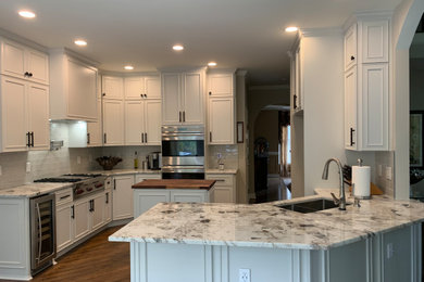Example of a mid-sized classic l-shaped medium tone wood floor and brown floor eat-in kitchen design in Atlanta with an undermount sink, recessed-panel cabinets, white cabinets, granite countertops, white backsplash, glass tile backsplash, stainless steel appliances, white countertops and an island
