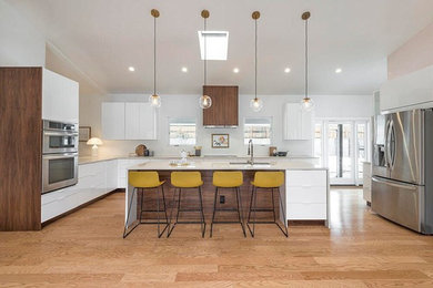 Example of a large 1960s light wood floor and vaulted ceiling eat-in kitchen design in Albuquerque with flat-panel cabinets, white cabinets, quartzite countertops, stainless steel appliances, an island and beige countertops
