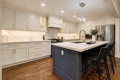 Example of a large transitional l-shaped medium tone wood floor, brown floor and coffered ceiling eat-in kitchen design in Toronto with an undermount sink, shaker cabinets, white cabinets, quartzite countertops, white backsplash, subway tile backsplash, stainless steel appliances, an island and white countertops