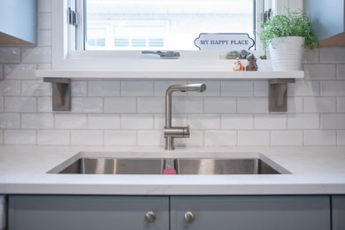 Example of a small trendy l-shaped open concept kitchen design in Other with an undermount sink, shaker cabinets, blue cabinets, quartz countertops, white backsplash, porcelain backsplash, stainless steel appliances, an island and white countertops