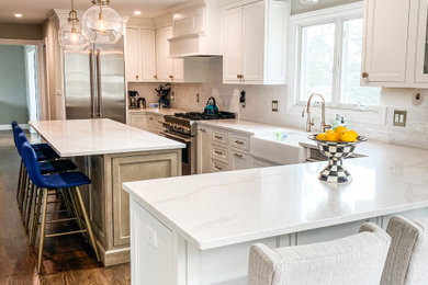Eat-in kitchen - mid-sized transitional u-shaped vinyl floor and beige floor eat-in kitchen idea in New York with a farmhouse sink, shaker cabinets, white cabinets, quartz countertops, white backsplash, glass tile backsplash, stainless steel appliances, an island and white countertops