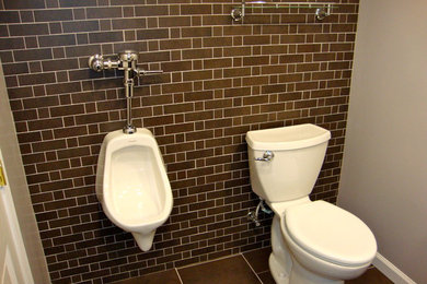 Photo of a mid-sized industrial powder room in Other with an urinal, recessed-panel cabinets, brown cabinets, grey walls, porcelain floors, an undermount sink, granite benchtops and brown floor.