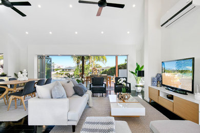 This is an example of a beach style formal open concept living room in Brisbane with white walls, a freestanding tv and black floor.
