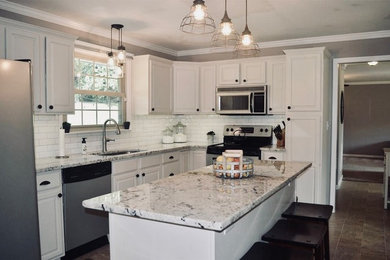 This is an example of a mid-sized transitional l-shaped open plan kitchen in Nashville with an undermount sink, raised-panel cabinets, white cabinets, granite benchtops, white splashback, subway tile splashback, stainless steel appliances, ceramic floors, with island, brown floor and beige benchtop.