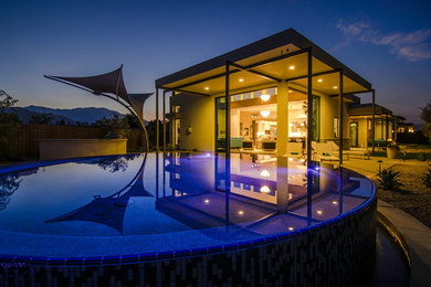 Example of a minimalist backyard concrete paver and round infinity pool design in Other