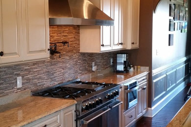 This is an example of a large transitional single-wall open plan kitchen in Philadelphia with an undermount sink, raised-panel cabinets, white cabinets, granite benchtops, beige splashback, ceramic splashback, stainless steel appliances, dark hardwood floors and multiple islands.