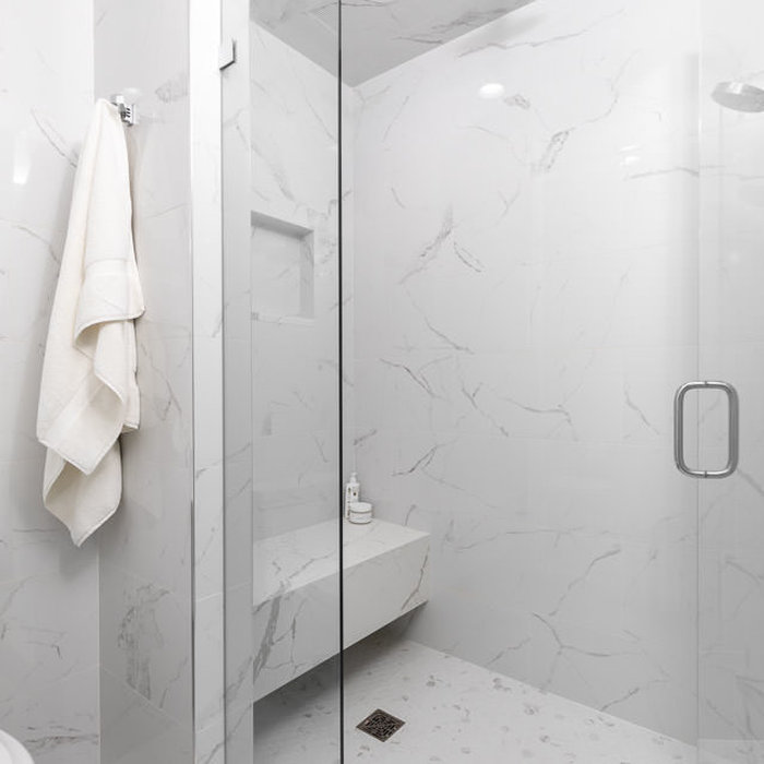 The master shower is built of large slab porcelain tile with a floating bench and shower niche above. The Hansgrohe Rain Shower Can creates a spa experience in this clean and  minimal space.