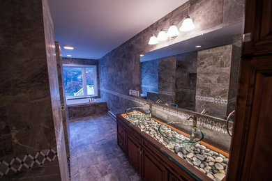 This is an example of a large transitional master bathroom in Philadelphia with raised-panel cabinets, medium wood cabinets, gray tile, porcelain tile, porcelain floors, an alcove tub, multi-coloured walls, a vessel sink and glass benchtops.