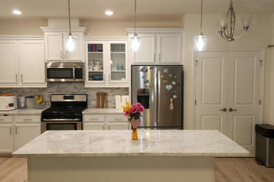 Mid-sized u-shaped laminate floor and beige floor kitchen pantry photo in Raleigh with a drop-in sink, white cabinets, granite countertops, white backsplash, ceramic backsplash, stainless steel appliances, an island and white countertops