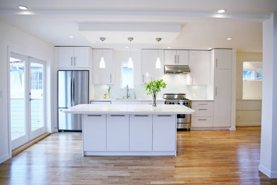 Mid-sized trendy single-wall light wood floor and beige floor open concept kitchen photo in Vancouver with a single-bowl sink, flat-panel cabinets, white cabinets, quartz countertops, white backsplash, glass sheet backsplash, stainless steel appliances and an island