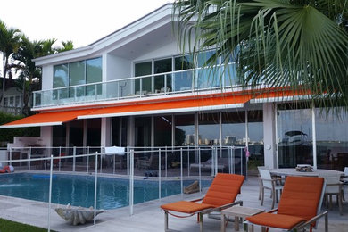 Photo of a large contemporary backyard patio in Miami with natural stone pavers and an awning.