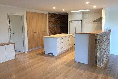 Mid-sized contemporary l-shaped open plan kitchen in Canberra - Queanbeyan with a drop-in sink, open cabinets, white cabinets, quartz benchtops, stainless steel appliances, light hardwood floors and with island.