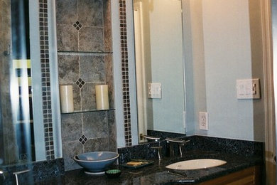 This is an example of a mid-sized asian bathroom in DC Metro with a drop-in sink, furniture-like cabinets, medium wood cabinets, granite benchtops, a corner shower, black tile, stone tile and white walls.